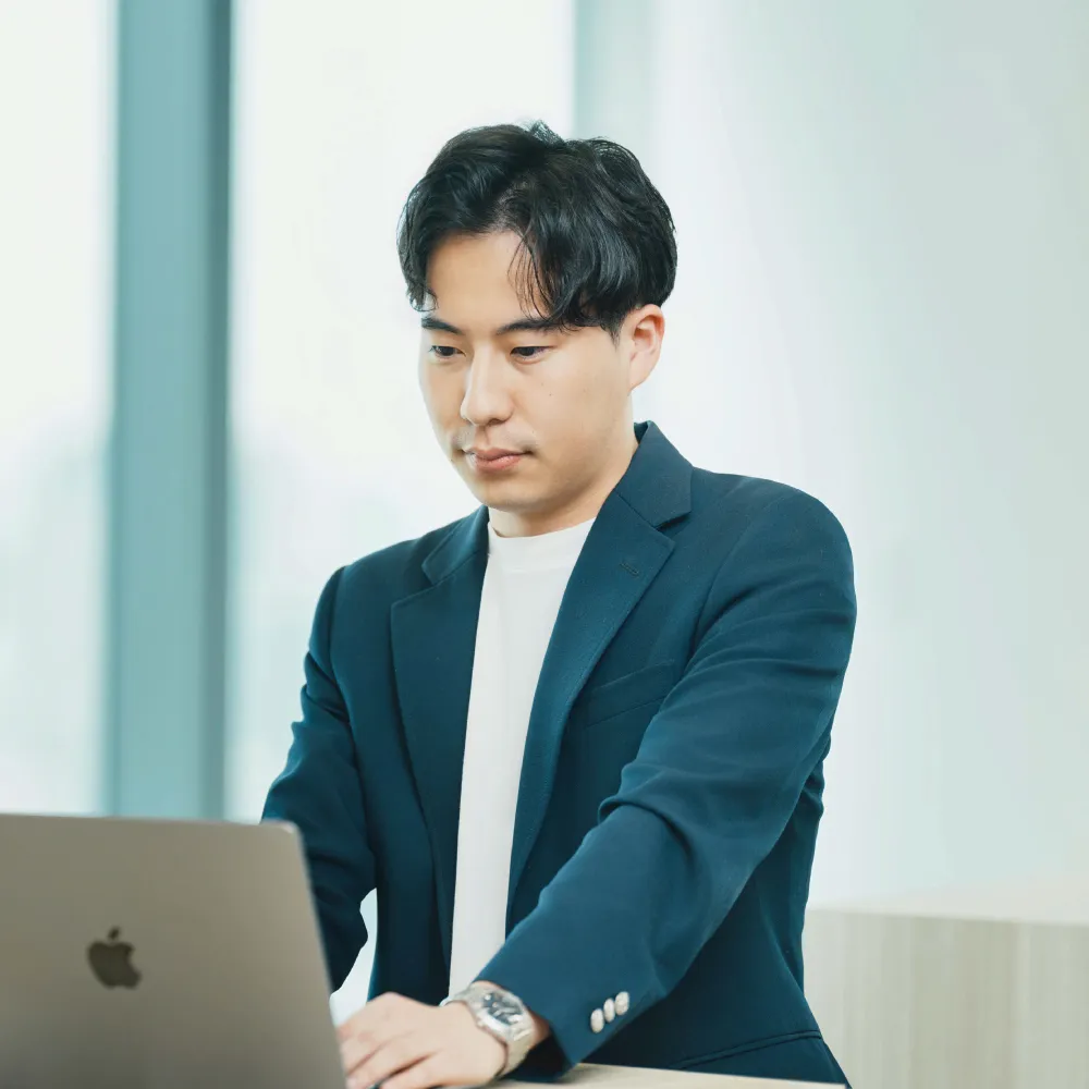 ノートパソコンで作業する紺色ジャケットの男性。