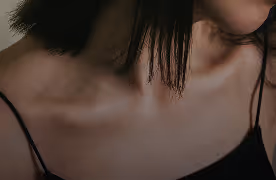 Close-up of a person’s collarbone and shoulders, with chin slightly lowered, wearing a thin-strapped top.