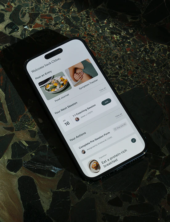 Smartphone displaying the WellTheory app dashboard with options for a food journal, symptom tracker, and upcoming coaching session.