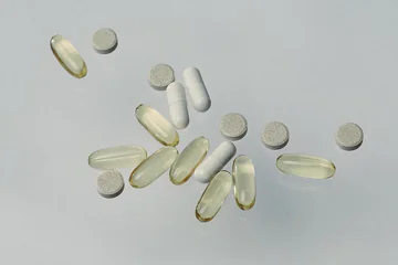 Assorted supplements including yellow softgels, white capsules, and round gray tablets on a light surface.