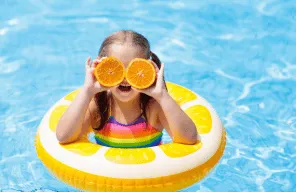 deklica na bazenu, šlauf/obroč in pomaranča. velik nasmeh
