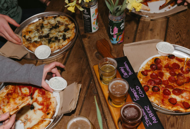 Image of three pizzas at a table with beer