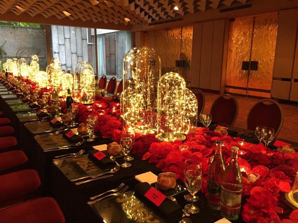 Aankleding van lange tafel met rood en glazen stulpen waar lichtjes in zitten.