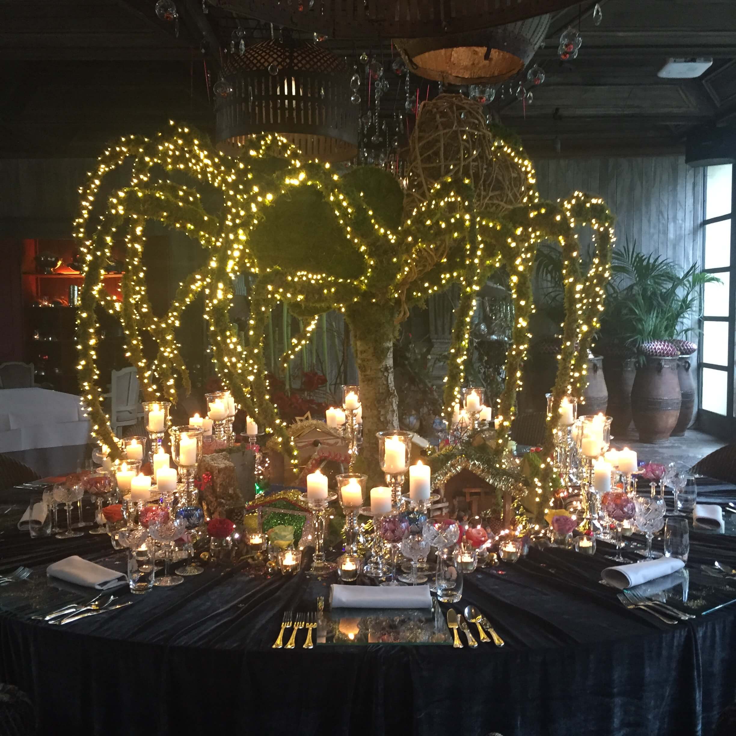 Evenement in Hof ten Damme met een grote ronde tafel. In het midden van de tafel staat een prachtig verlichte boom met hangende takken.