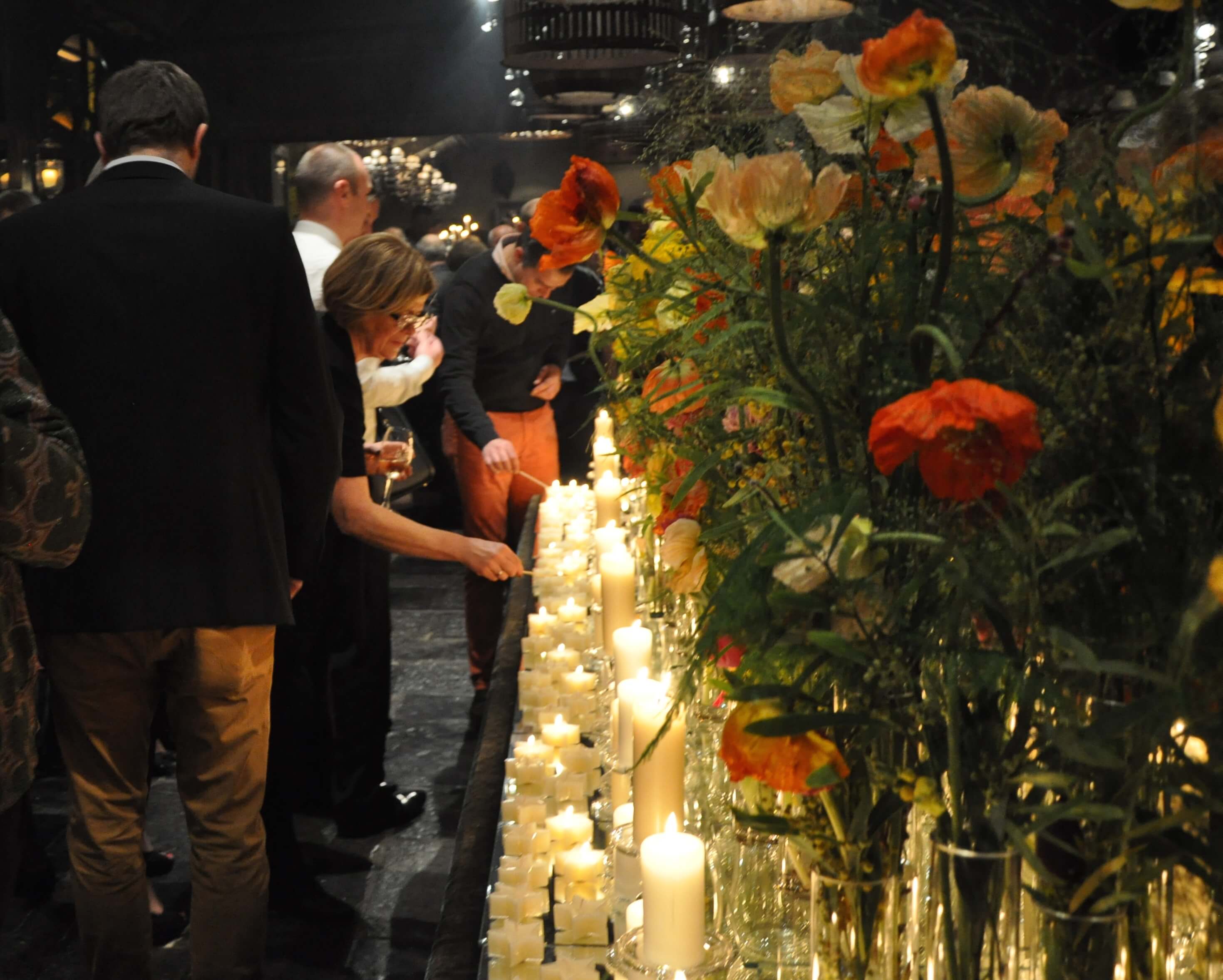 Vrouw steekt kaarsje aan op lange tafel vol met kaarsen tijdens een event.