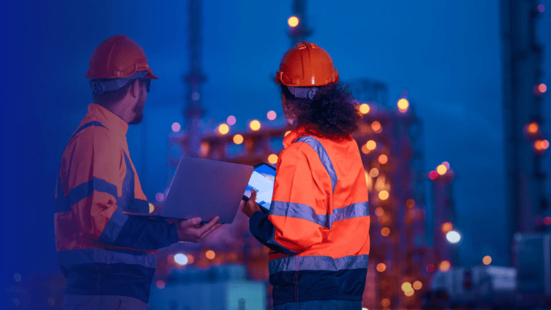 Two workers in safety gear using laptops at a construction site, highlighting SaaS security in industrial settings.