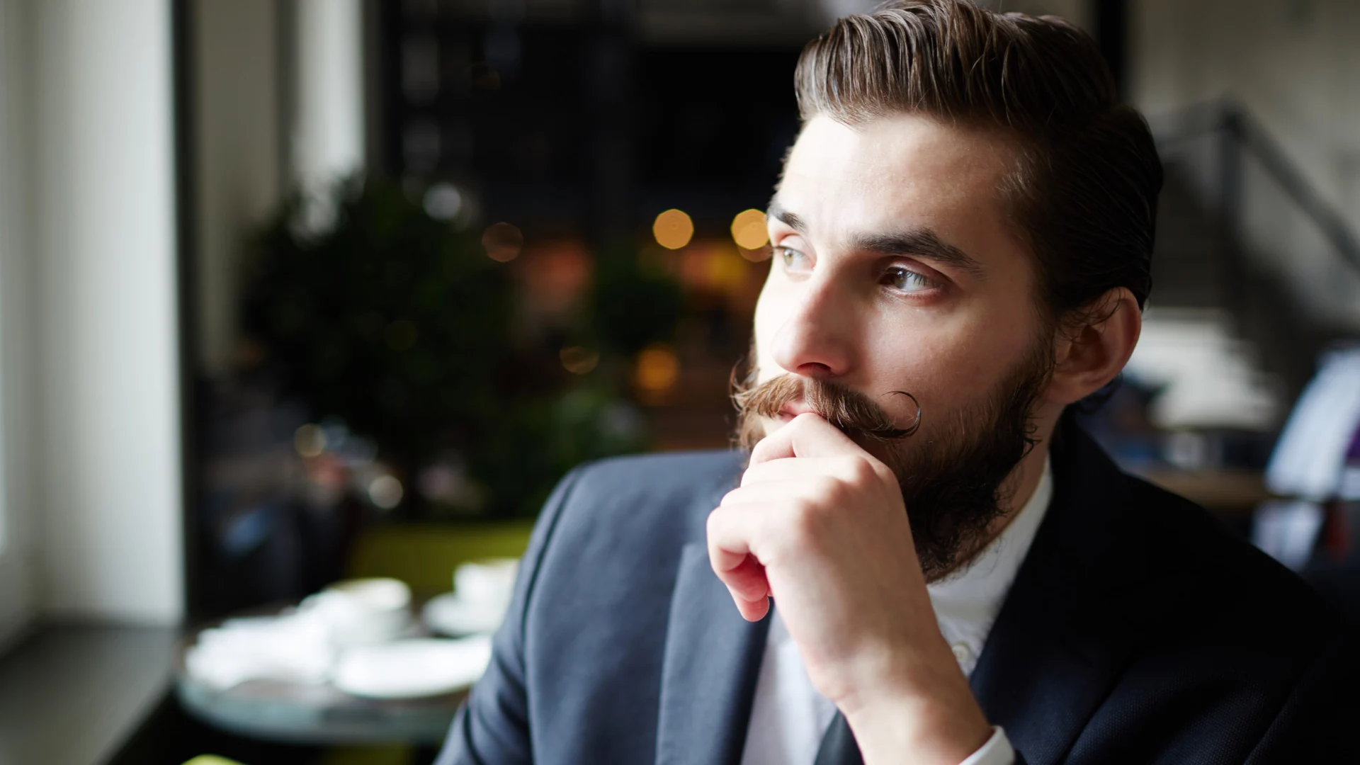 Thoughtful man in a suit contemplating SaaS security solutions in a modern cafe setting.