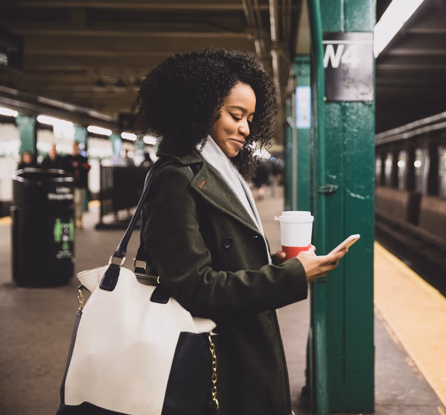A woman looking at her phone, waiting for the subway