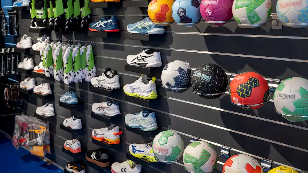 Sportgeschäftwand mit angeordneten Sportschuhen, Handbällen und Sportzubehör.