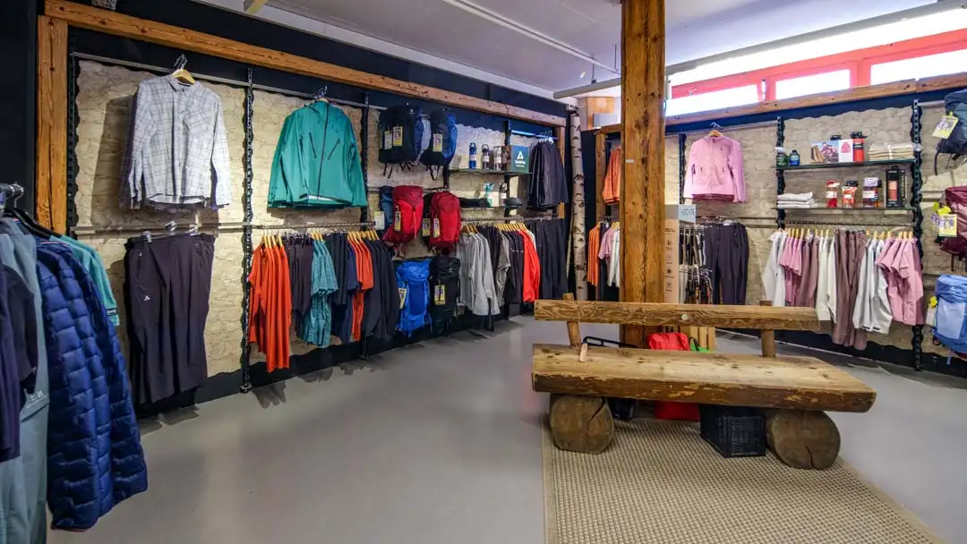 Inneneinrichtung eines Sportgeschäfts mit Outdoor-Bekleidung, Rucksäcken und einer Holzbank in der Mitte.