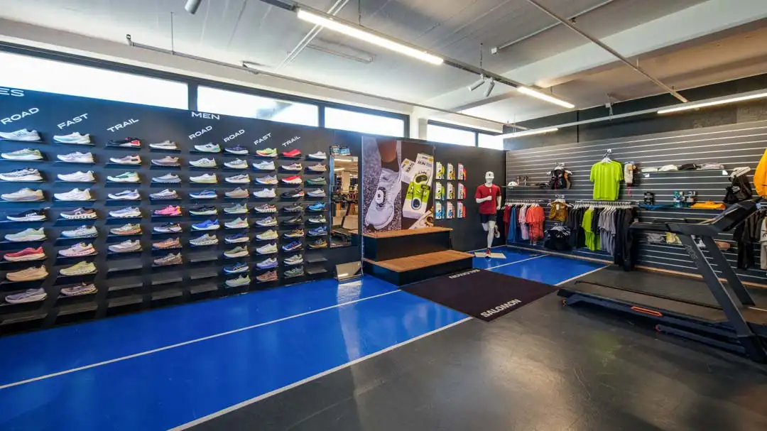 Innenraum eines Sportgeschäfts mit Laufschuhen an der Wand, Bekleidung und einem Laufband.