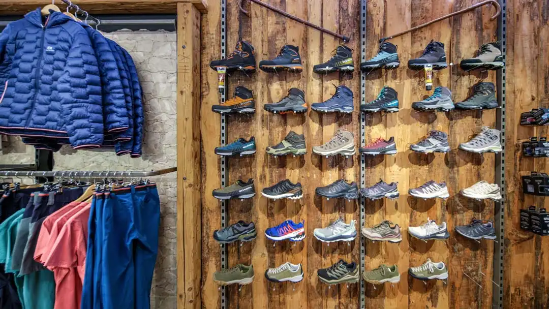 Wand mit verschiedenen Wanderschuhen und Outdoorbekleidung in einem Geschäft.