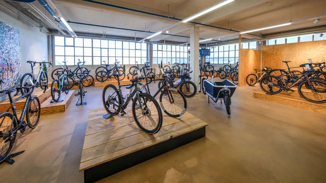 Fahrradgeschäft mit Rennrädern und Lastenfahrrad auf Holzplattformen in hellem Raum.