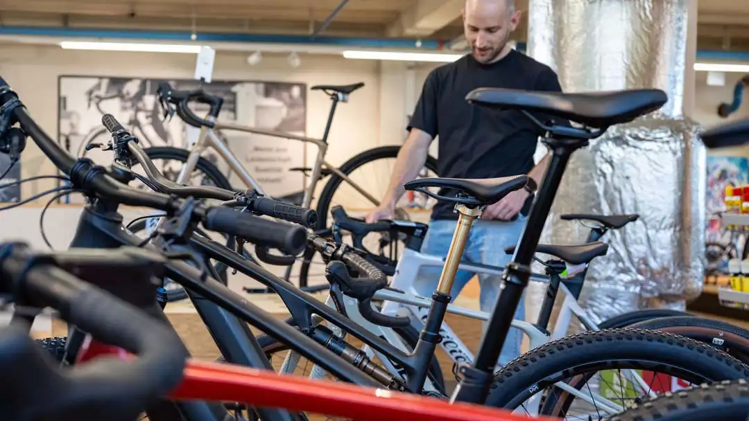 Mann betrachtet verschiedene Mountainbikes in einem modernen Fahrradladen mit hellem Hintergrund.
