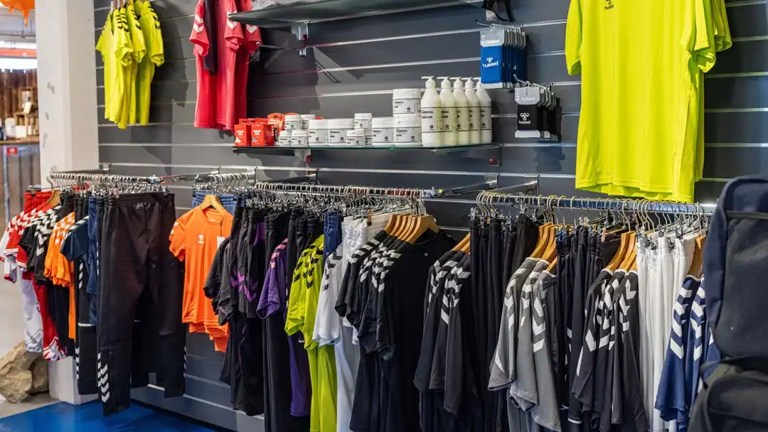 Sportbekleidung wie T-Shirts und Hosen hängen ordentlich auf Stangen in einem Geschäft.