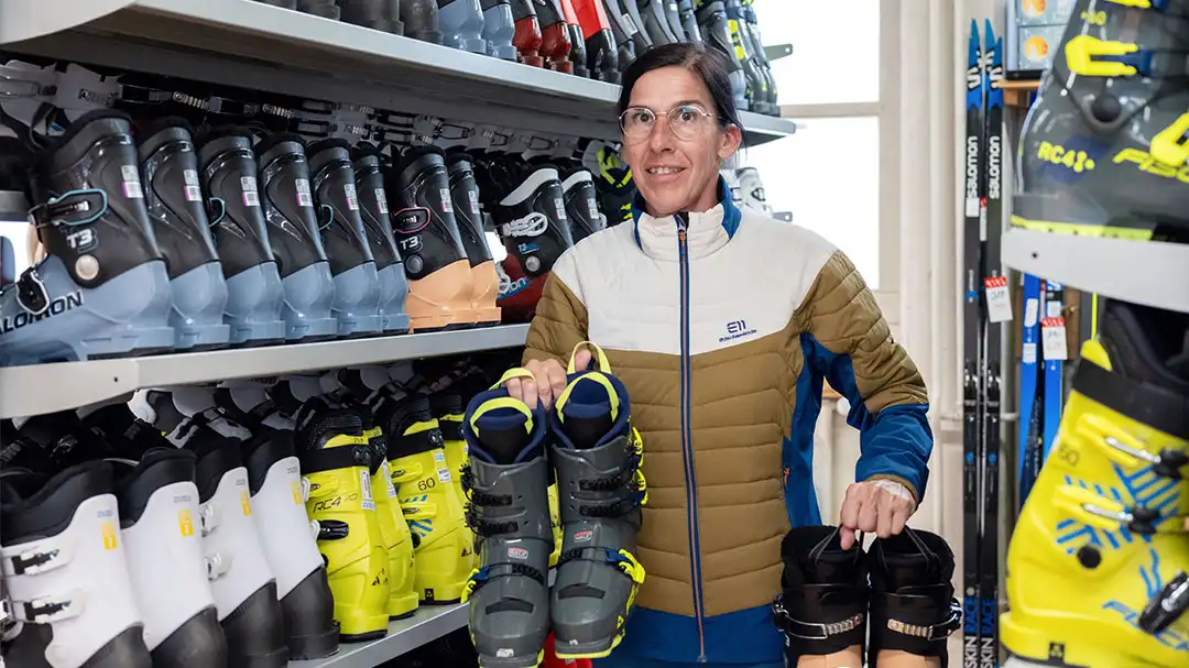 Frau in Ski-Geschäft hält Paar Skischuhe in jeder Hand, umgeben von Regalen voller Skistiefel.