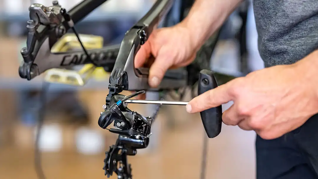 Techniker justiert mit Schraubenzieher die Schaltung eines Fahrrads ohne Laufräder.