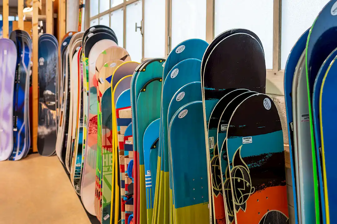 Reihe von bunten Snowboards steht in einem Raum vor Fenstern, bereit für den Verleih oder Verkauf.