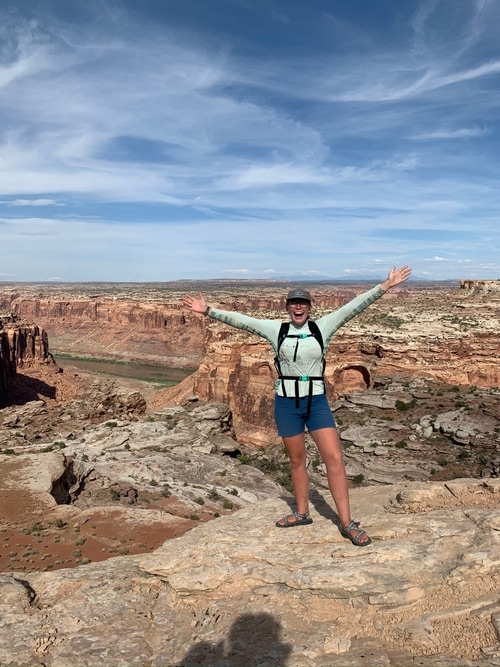 person posing with arms in the air near canyon edge and the river down below