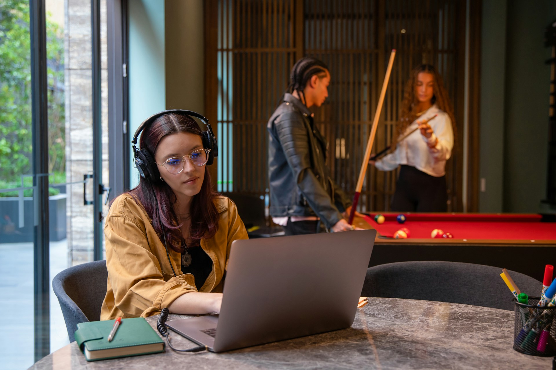a woman working while two others playing pool in the back