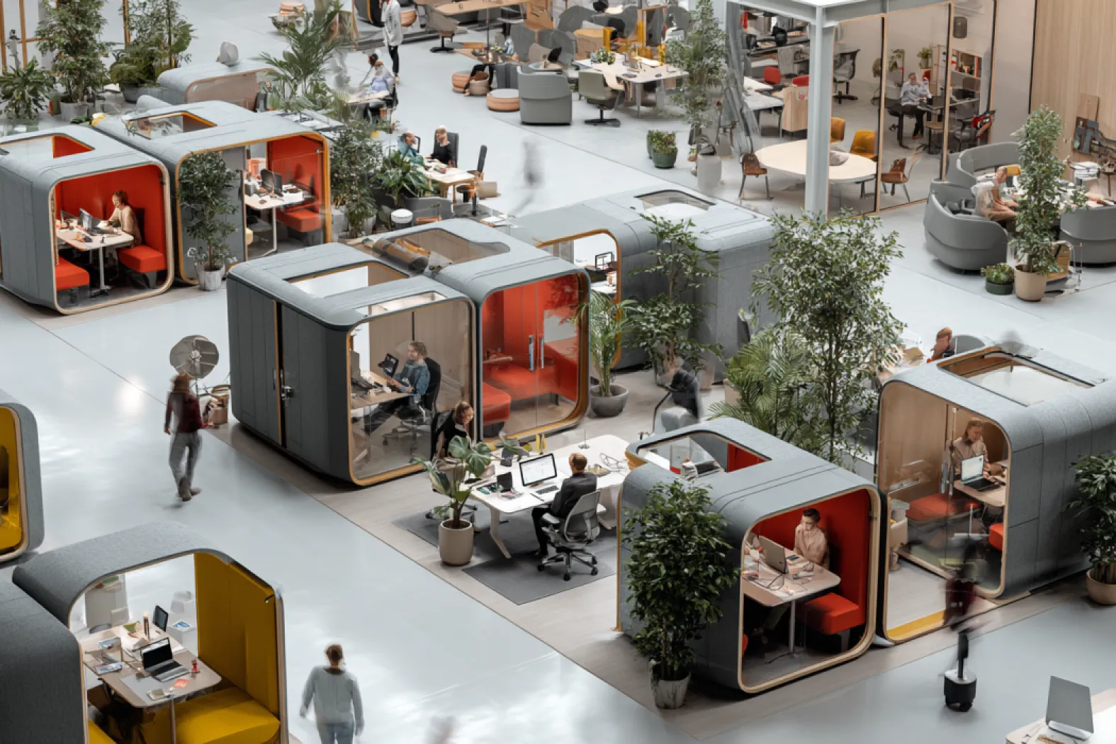 Modern open workspace with private pods and people working at desks surrounded by plants.