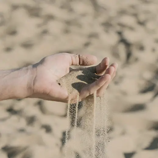 Sand rinnt durch eine Hand am Strand – Symbol für Vergänglichkeit bei einer Meer- oder Seebestattung