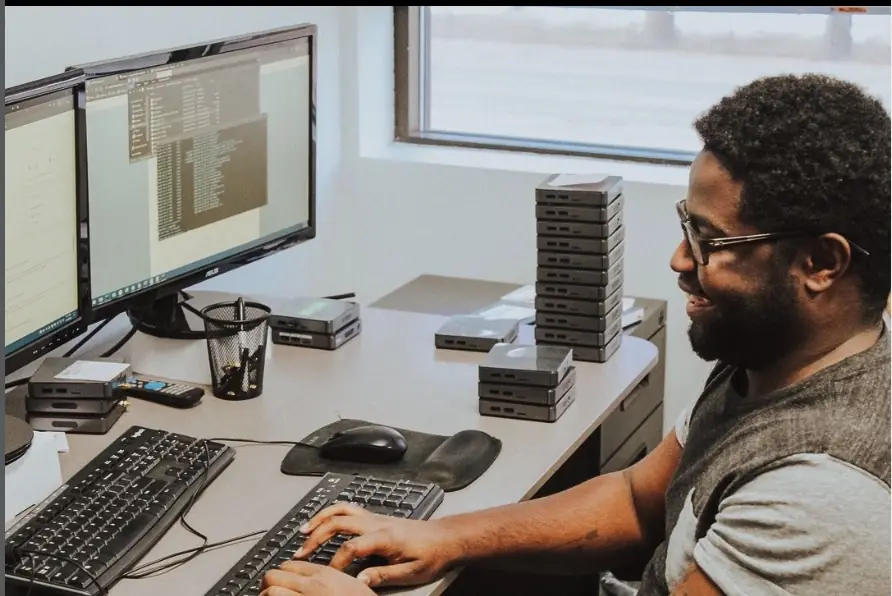 A truDigital technician staging and pre-pairing sign players at a desk in Sandy, Utah, with stacks of players ready to ship.