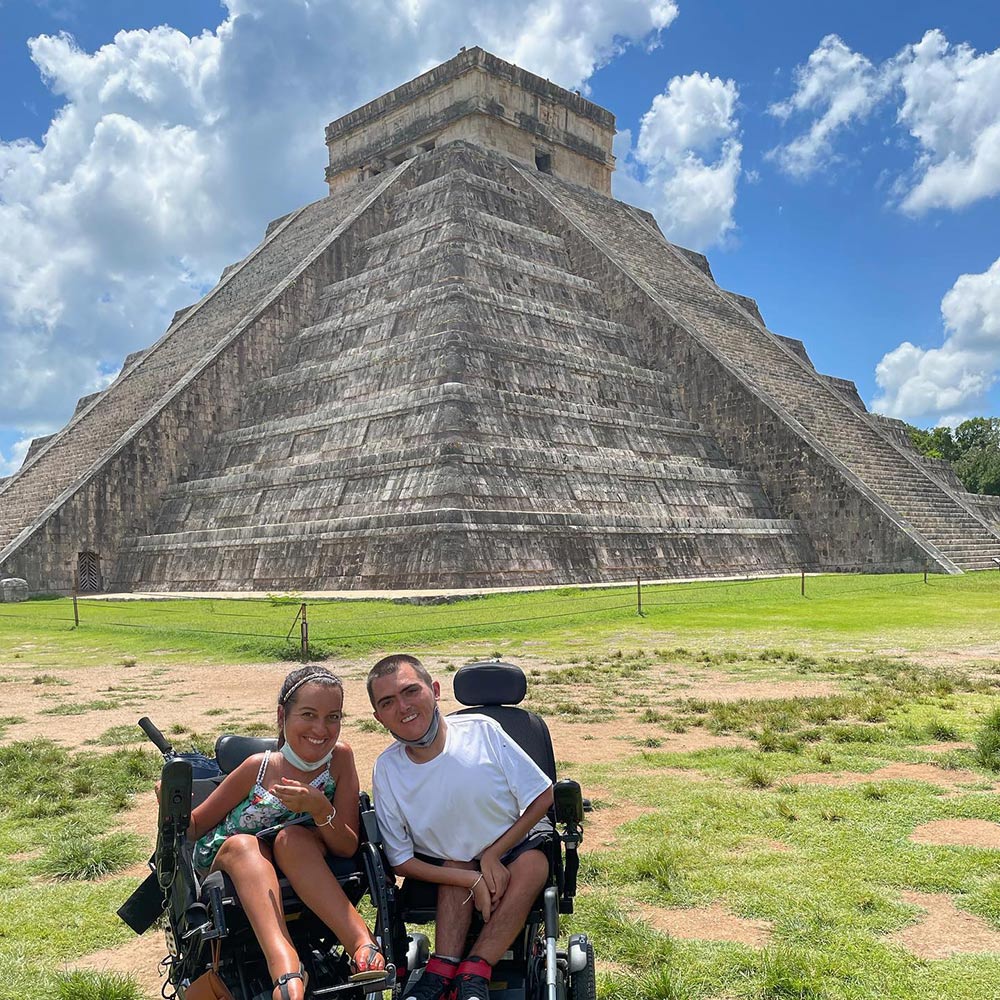 A man and a little girl sitting in a wheel chair in front of a pyramid.