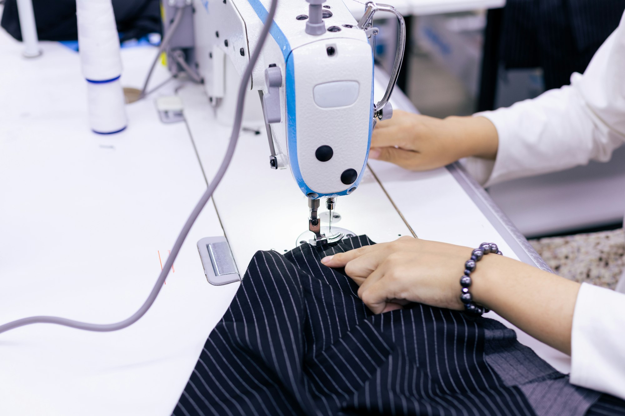 Hands guiding pinstriped fabric through a sewing machine