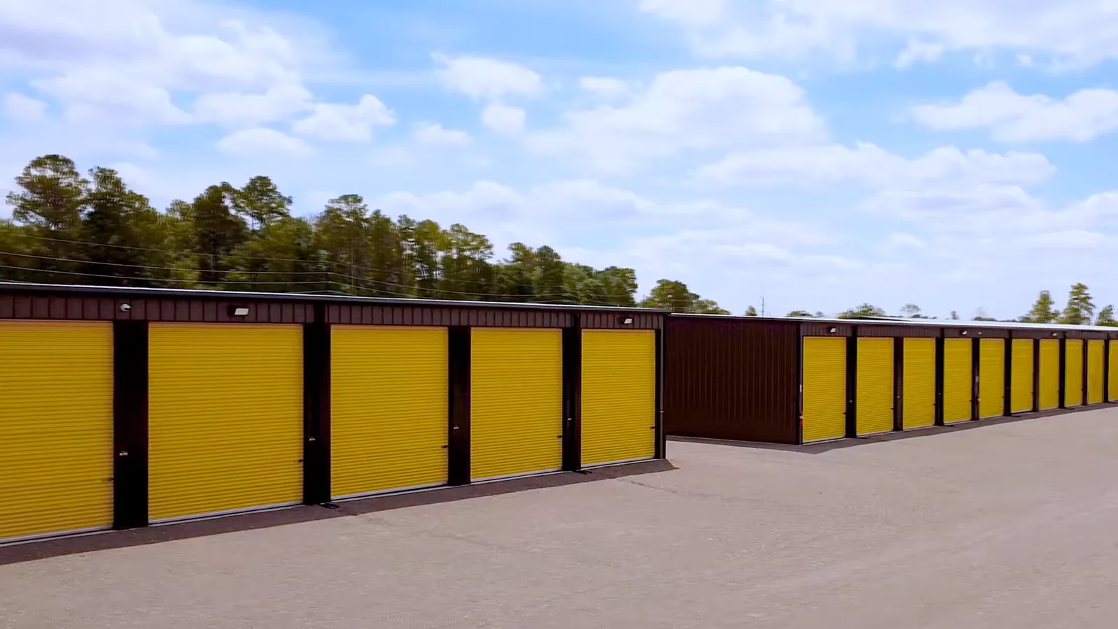Enclosed storage buildings with yellow roll-up doors under a blue sky at Foxgate Boat & RV Storage