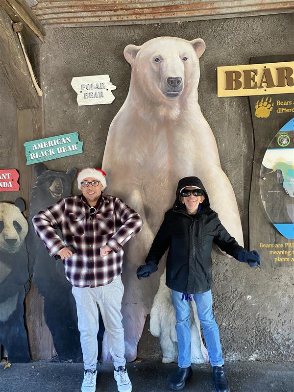 Two people posing with arms bent to mimic a large painted polar bear and other bear illustrations on a textured wall.