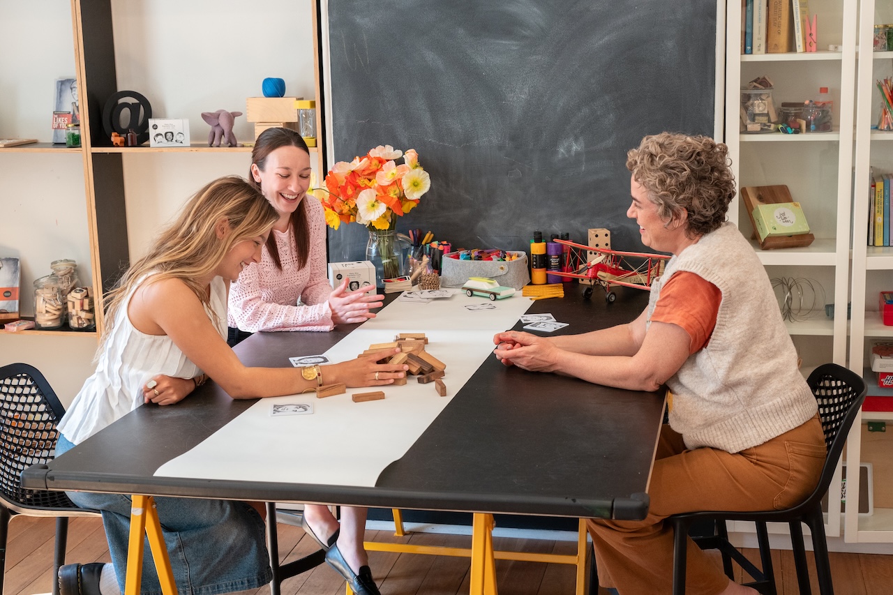 Three psychologists sitting at a therapy table in a child-friendly clinic, engaging with educational cards and blocks during a playful, supportive psychology session at Quirky Kid Woollahra.