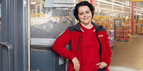 Eine Frau, sie lächelt und steht in einer Verteilzentrale