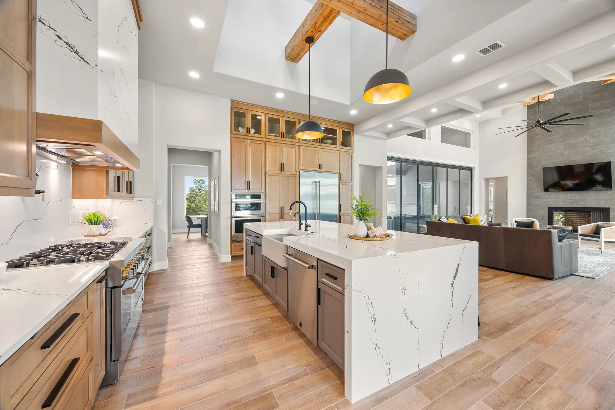 Spacious modern kitchen and open-concept living area in a luxury custom home by KC Custom Homes in Pecan Springs near Boerne, TX, featuring waterfall quartz island and wood accents.