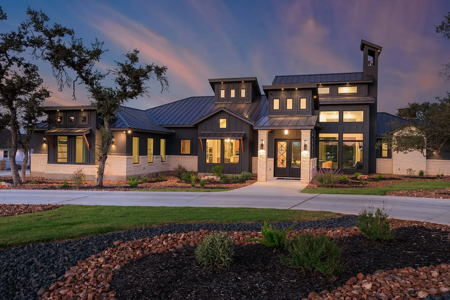 Modern Hill Country home exterior with black metal roof, limestone accents, and large windows built by KC Custom Homes