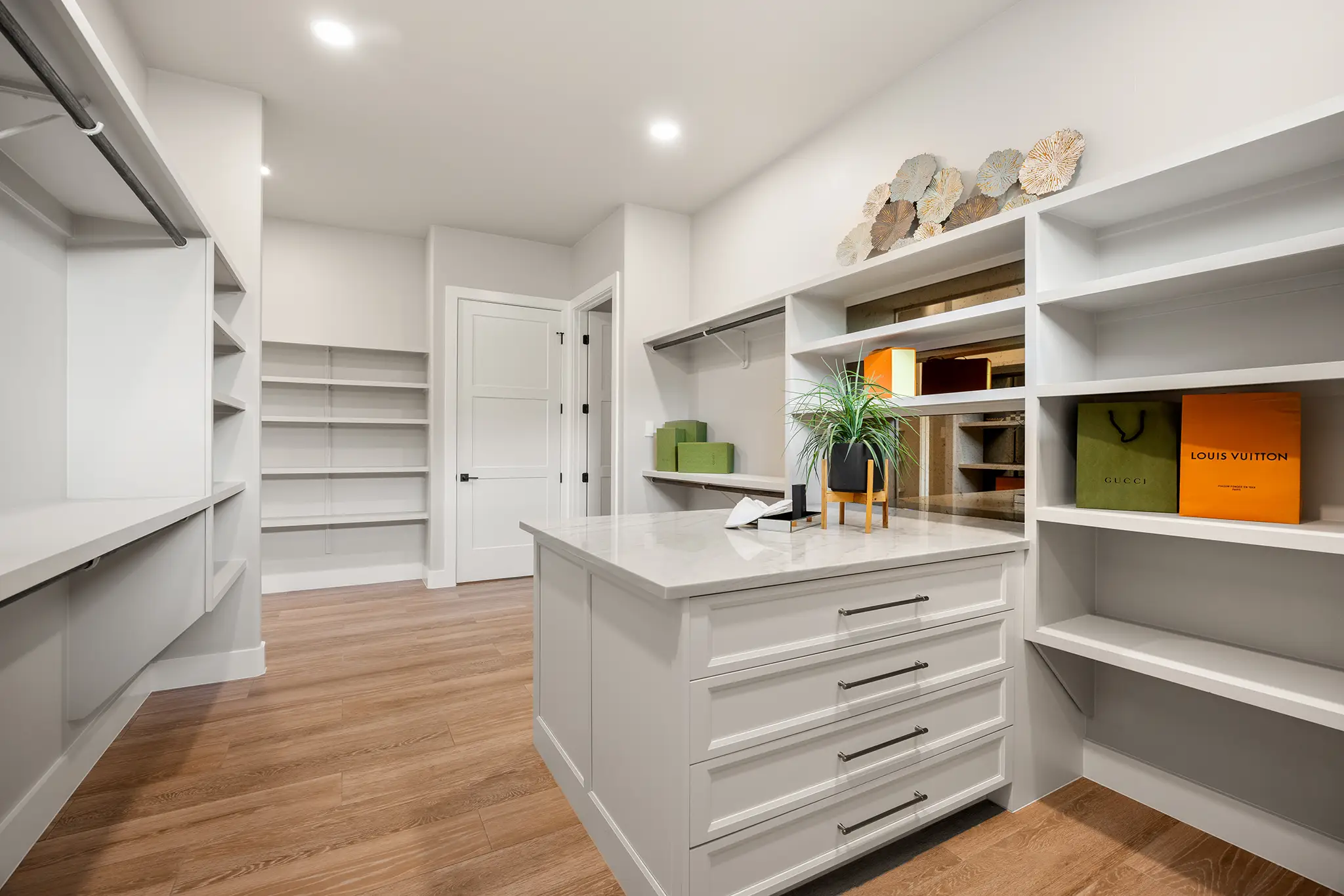 Spacious custom walk in closet in a KC Custom Homes residence with built in white shelving, center island with marble top, wood flooring, and designer storage accents in New Braunfels Texas.
