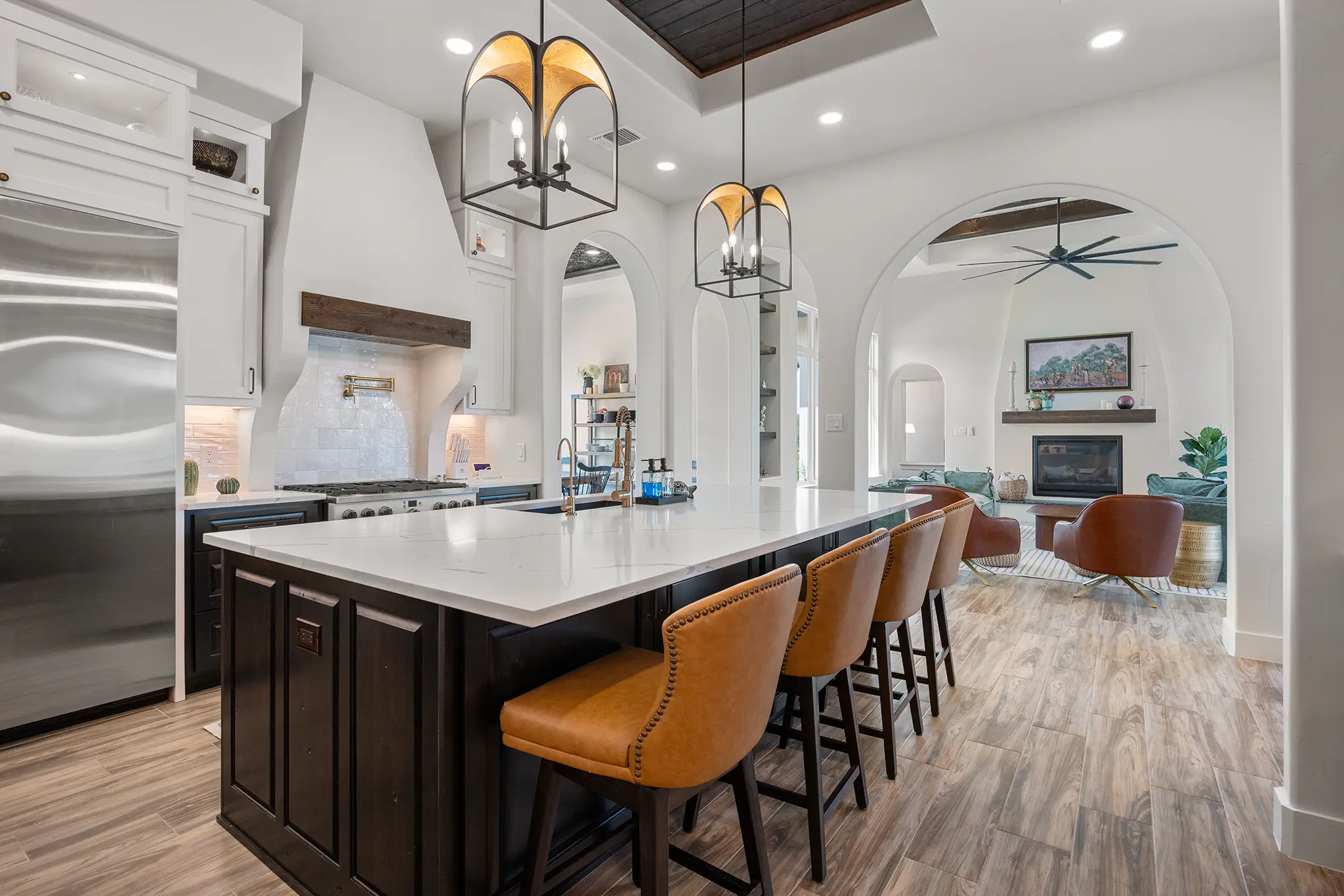 Gourmet kitchen with a large island, leather barstools, arched openings, custom cabinetry, and pendant lighting in a Mitchell Ranch custom home in Bulverde Texas.