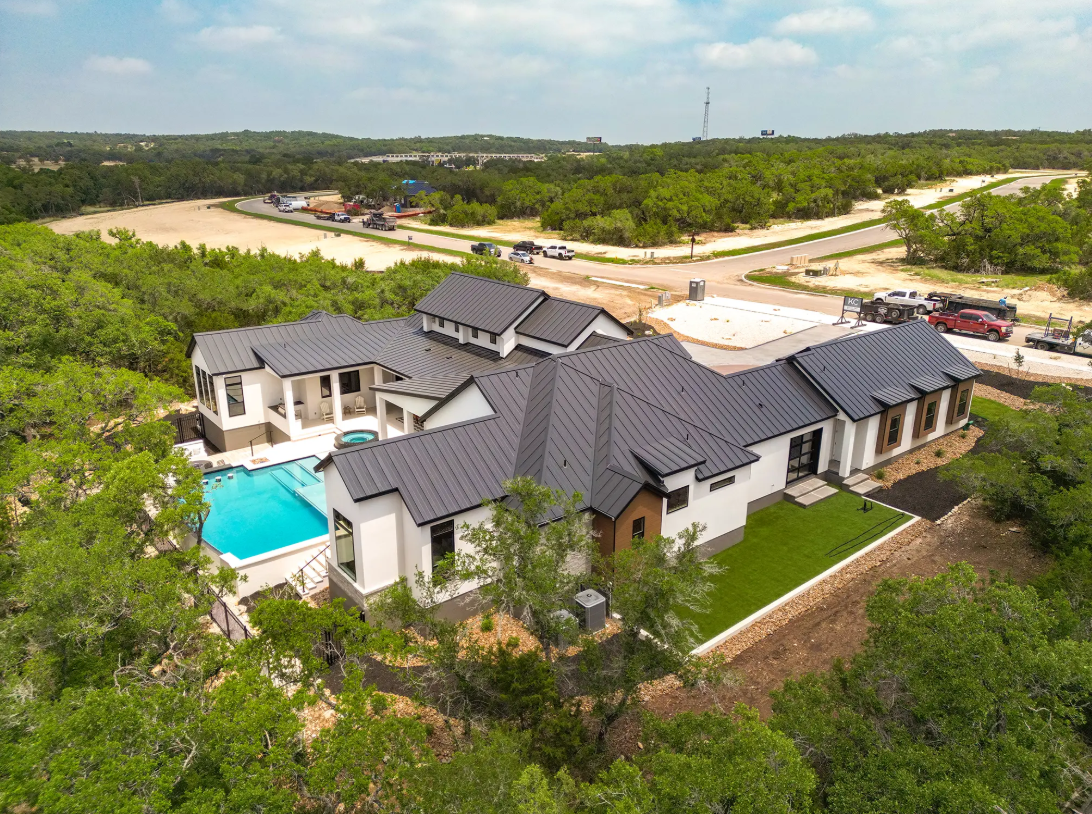 Modern farmhouse custom build with swimming pool and black standing seam metal roof on a wooded lot in the Texas Hill Country.