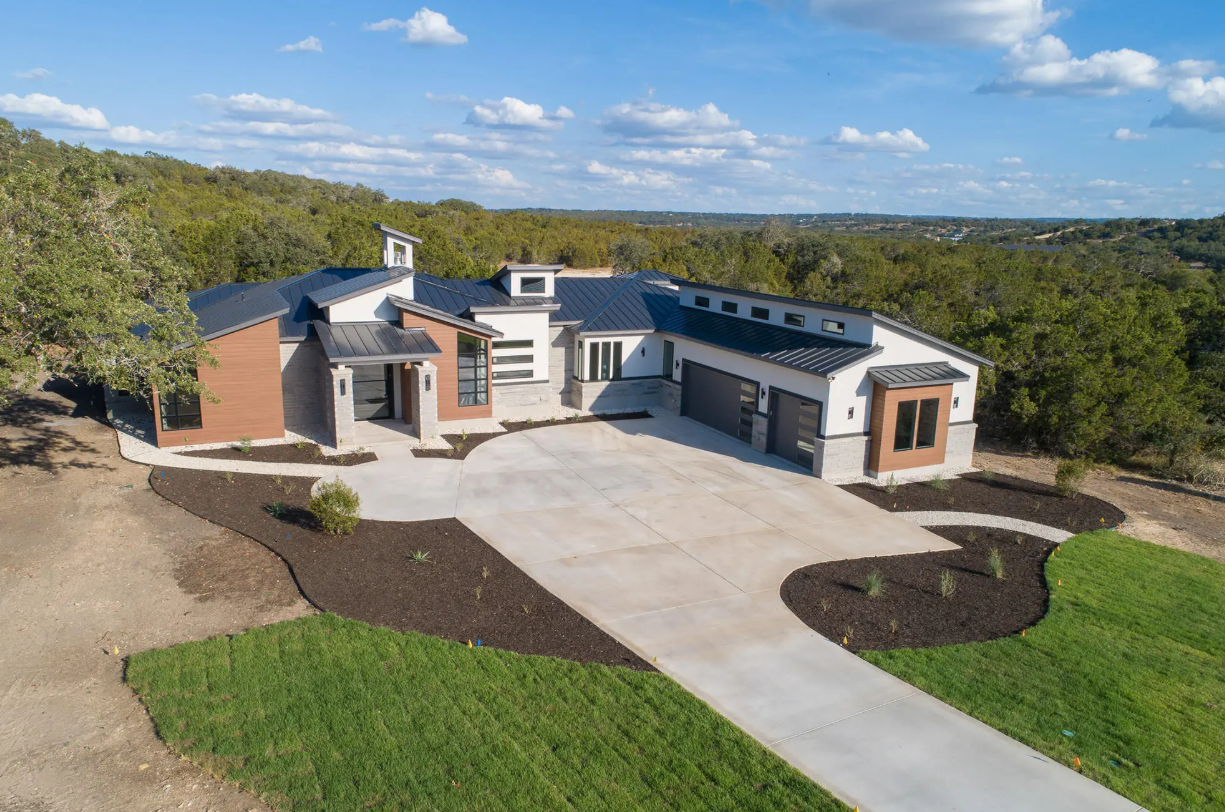 Front exterior of a contemporary custom home featuring wood siding, stone accents, and a circular driveway built by KC Custom Homes.