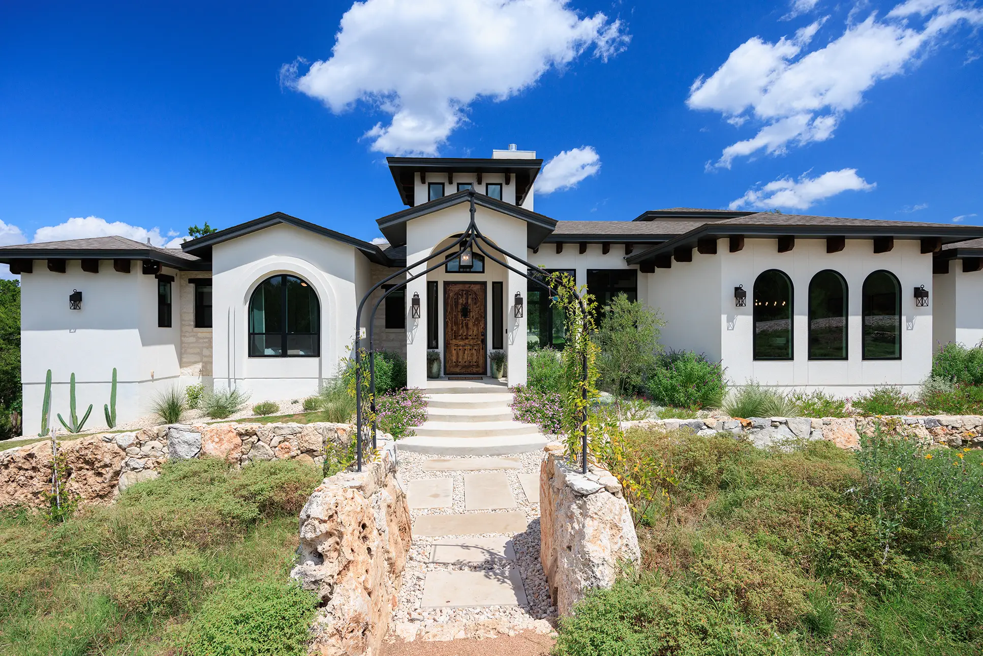 Spanish-style custom estate in New Braunfels featuring white stucco, arched black-frame windows, and a custom iron entry door.