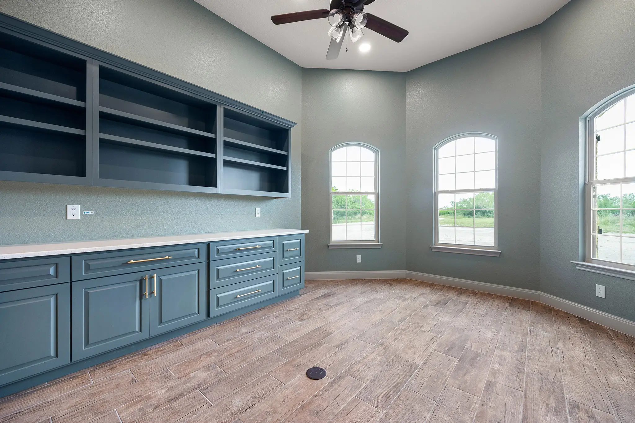 Custom home office with teal blue floor-to-ceiling built-in cabinetry and large arched windows for natural light.
