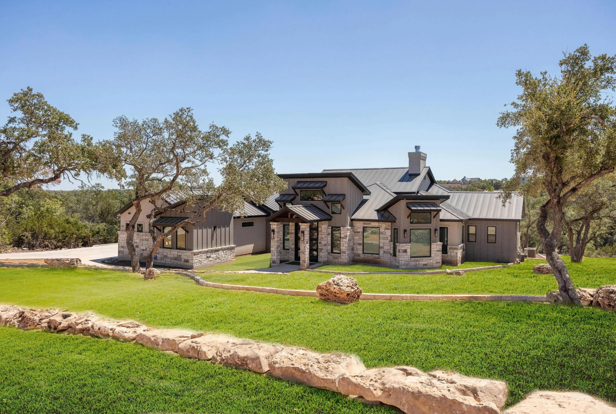 A luxury custom home featuring native limestone exterior architecture seamlessly integrated into a sloped hillside terrain in Comal County.