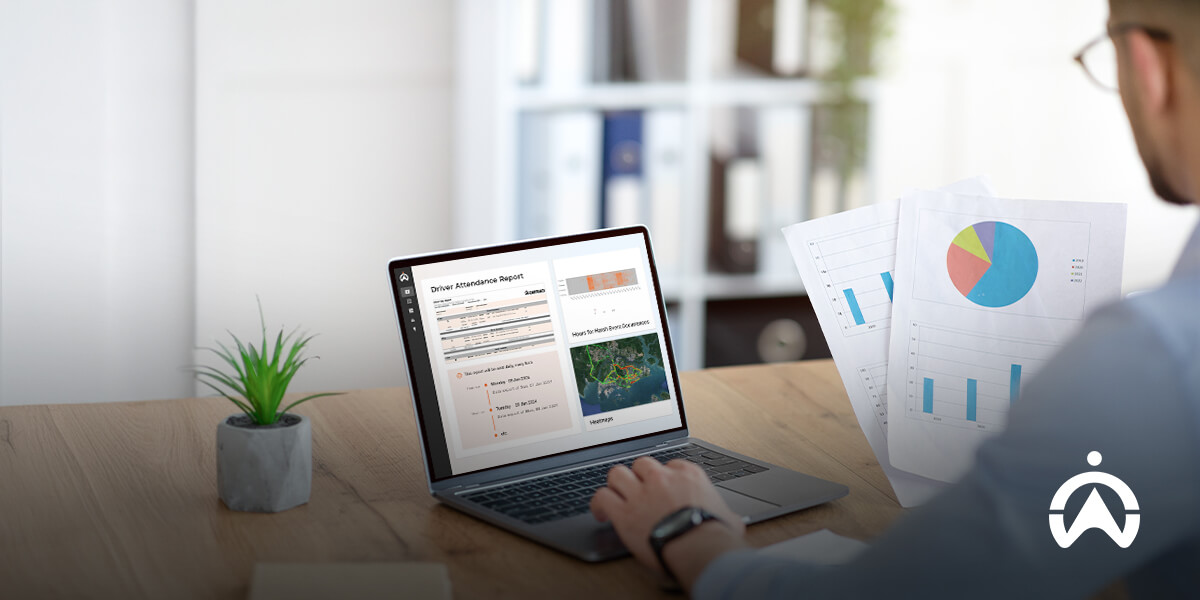 Cartrack driver scorecards on laptop with attendance report, charts, and plant on wooden table.