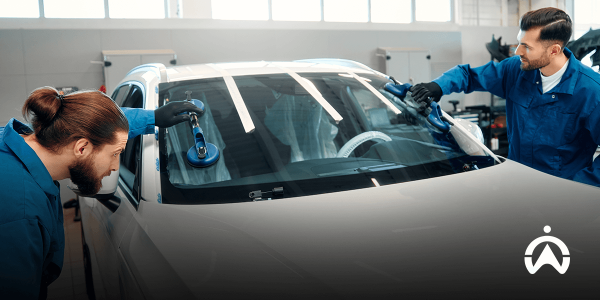 Two technicians repairing a car windshield in an auto shop.