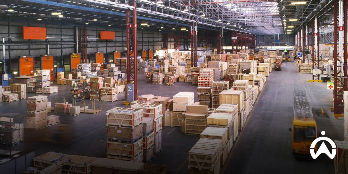 A spacious warehouse filled with stacked wooden crates, organized rows, and loading docks visible in the background.