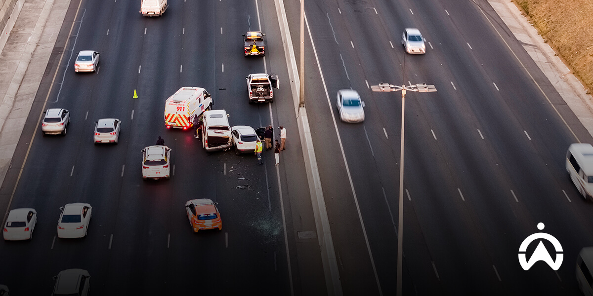 Emergency responders assist at a multi-car accident on a busy highway, with damaged vehicles and a police presence visible.