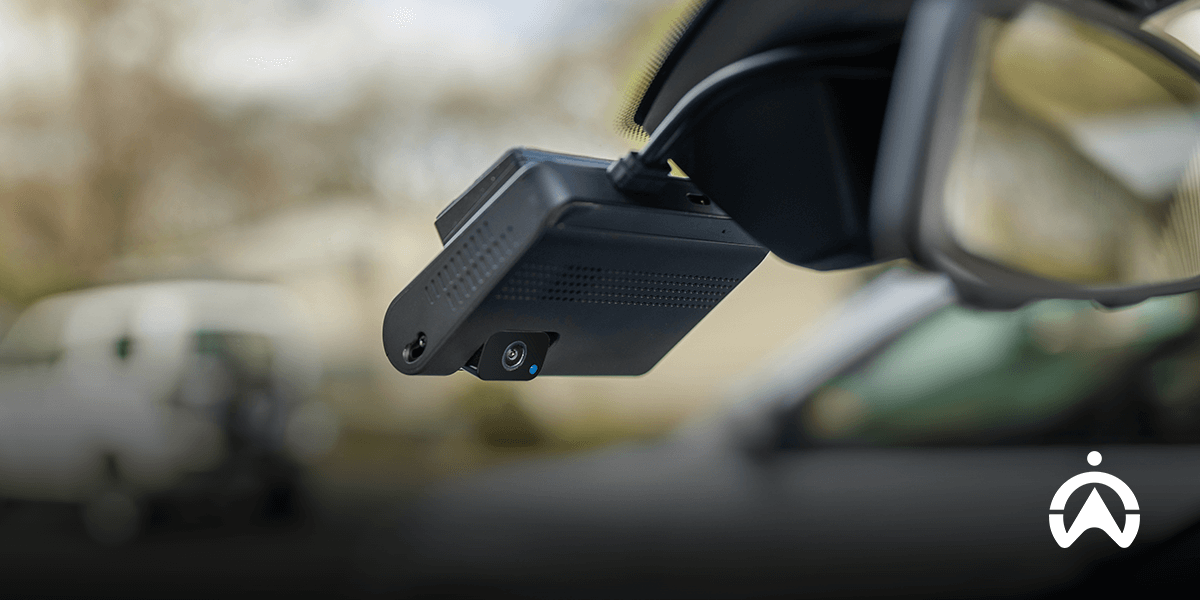 A mounted Cartrack dashcam, capturing the view through the windshield, with a blurred background of a vehicle and trees outside.