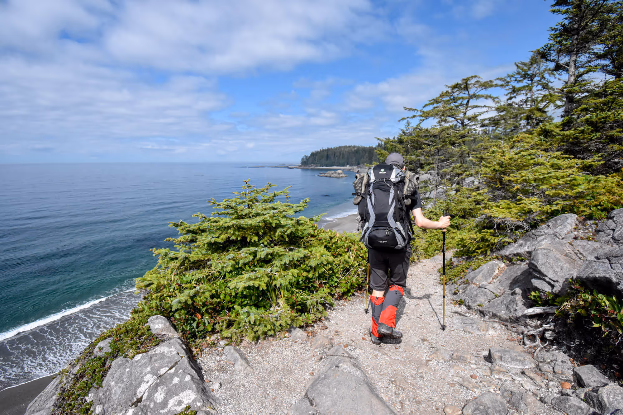 hiker on trail beside a cliff alongside the ocean on the west coast trail