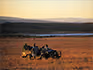 A safari vehicle parked in an open field for a sundowner with water and hills in the distance. 