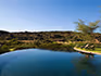 Two people sun bathing on loungers on the edge of a flow rim swimming pool surrounded by nature. 